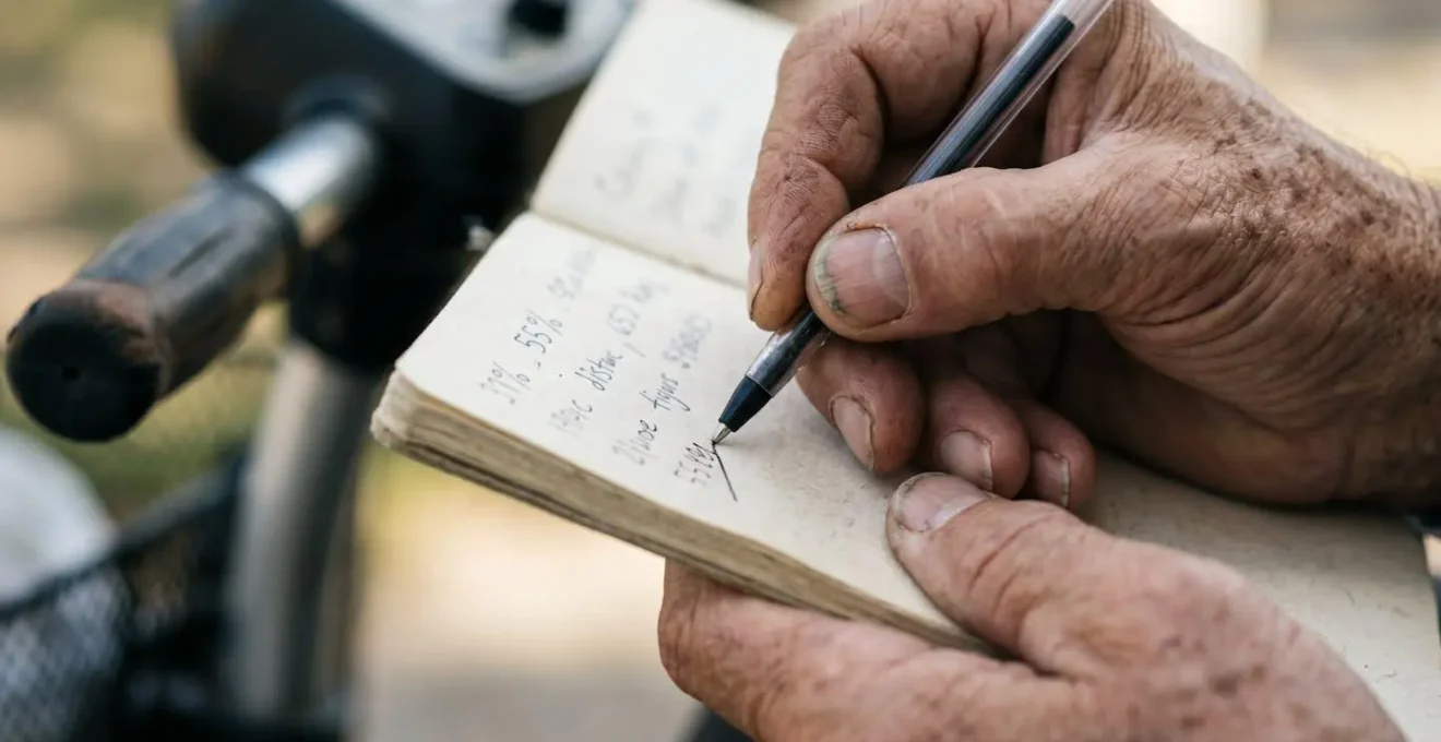 Close-up of hands recording battery data during mobility scooter range testing on notebook